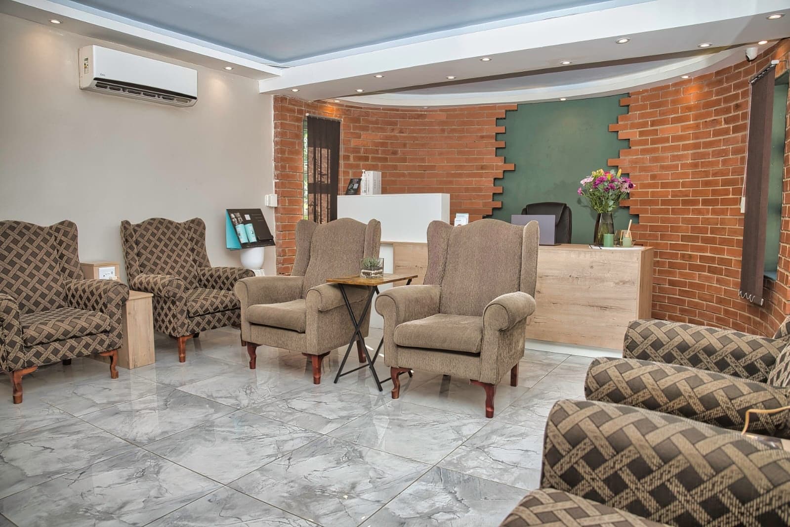 The waiting room at the Phoenix practice: rows of upholstered wing-back armchairs on a marble floor, with a brick feature wall and the reception desk behind.